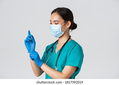 Covid-19, Coronavirus Disease, Healthcare Workers Concept. Professional Smiling Asian Female Nurse, Physician In Scrubs And Medical Mask Put On Rubber Gloves For Checkup, Patient Examination