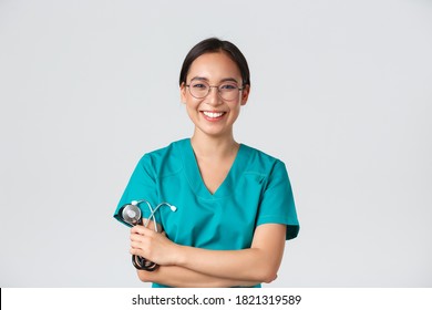 Covid-19, coronavirus disease, healthcare workers concept. Confident happy asian female physician, doctor in glasses, cross arms chest and smiling, holding stethoscope for examination