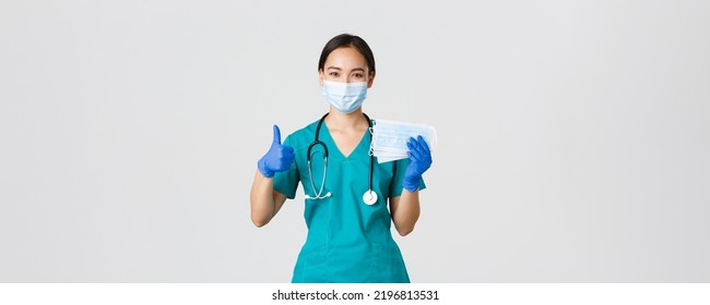 Covid-19, Coronavirus Disease, Healthcare Workers Concept. Smiling Asian Doctor, Nurse In Scrubs And Rubber Gloves, Showing Thumbs-up And Medical Masks, White Background