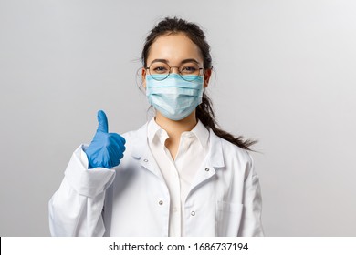 Covid19, coronavirus, healthcare and doctors concept. Portrait of optimistic asian female doctor assure everything be okay, thumb-up, wear medical mask to prevent catching virus, white coat