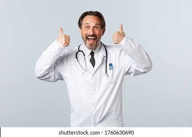 Covid-19, coronavirus outbreak, healthcare workers and pandemic concept. Excited upbeat male doctor in white coat thumbs-up in approval. Surgeon agree or like idea, recommend promo - Shutterstock ID 1760630690
