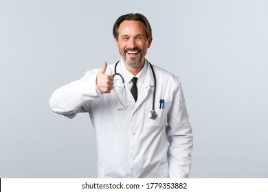 Covid-19, coronavirus outbreak, healthcare workers and pandemic concept. Handsome cheerful male doctor in white coat show thumbs-up in approval, agree or like product, recommending - Powered by Shutterstock