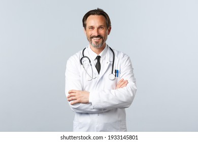 Covid-19, coronavirus outbreak, healthcare workers and pandemic concept. Enthusiastic smiling doctor, physician in white coat looking enthusiastic, cross arms chest, listening to patient