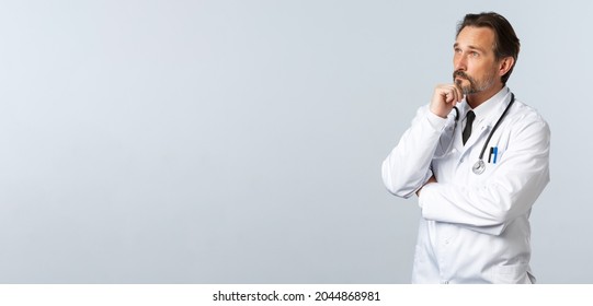 Covid-19, coronavirus outbreak, healthcare workers and pandemic concept. Thoughtful therapist, male doctor in white coat making decision, solving disease case in hospital, thinking as looking left - Powered by Shutterstock