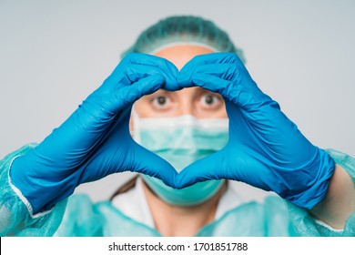 COVID-19 Coronavirus Pandemic Happy Woman Doctor Positive With A Medical Mask And Hands In Latex Glove Shows The Symbol Of The Heart. Doctor For The Heart. Love Our Medical Professionals.