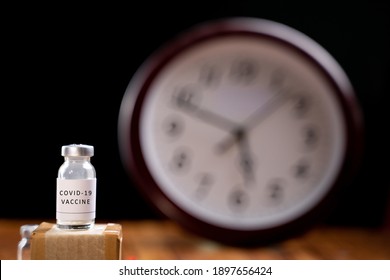 Covid-19 Coronavirus Vaccination Bottle With Clock Behind, Concept Of Covid-19 Vaccine Immunity Duration And Second Dose Time Frame