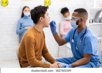 Covid-19 Diagnostic. African American Doctor Testing Sick Asian Patient For Coronavirus Using Throat Swab Sitting In Clinic Indoors. Corona Virus Test And Treatment Concept - Shutterstock ID 1827501599