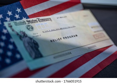 COVID-19 Economic Stimulus Check On Blurred USA Flag And Sun Light Background. Relief Program Concept. 