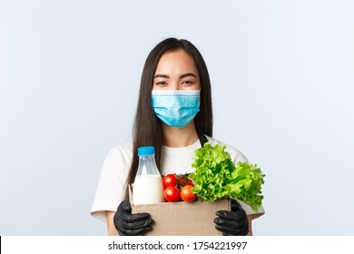 Covid-19, Grocery Store, Employment, Small Business And Preventing Virus Concept. Cheerful Smiling Asian Cashier, Shop Worker In Medical Mask And Gloves Holding Products Order In Bag