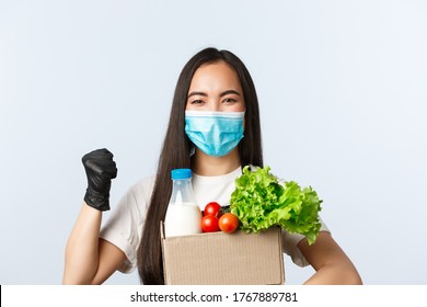 Covid-19, Grocery Store, Employment, Small Business And Virus Concept. Enthusiastic Asian Female Employee, Shop Cashier In Medical Mask, Fist Pump Encourage Buy Safe, Giving Bag With Groceries