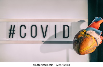 COVID-19 Hashtag Sign Next To Medical Heart Model Showing Cardiovascular Risk Of Stroke Blood Clot With Coronavirus Infection. Lightbox Billboard Text.