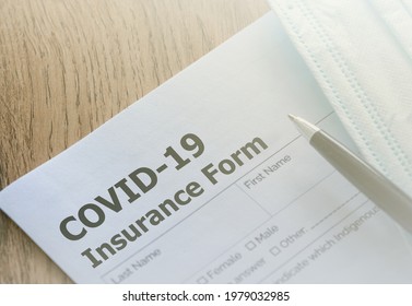 COVID-19 Health insurance paper form with a pen and medical mask on wooden table. Health insurance concept. 