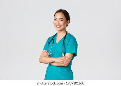 Covid-19, healthcare workers, pandemic concept. Professional confident, smiling asian female doctor, nurse in scrubs with stethoscope for examinations, cross arms and look at camera