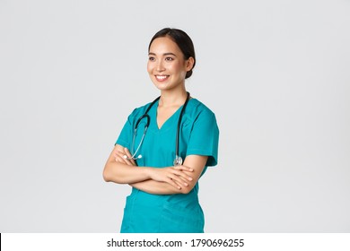 Covid-19, Healthcare Workers, Pandemic Concept. Side View Of Professional Confident And Hopeful Asian Female Doctor, Nurse Looking Assured Away And Smiling, Standing In Scrubs White Background