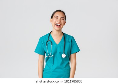 Covid-19, Healthcare Workers, Pandemic Concept. Carefree Beautiful Female Asian Nurse In Scrubs, Intern Having Fun, Laughing Happy. Doctor On Lunch Break Chuckle And Talking To Coworkers