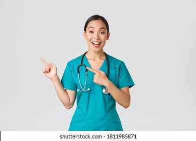 Covid-19, healthcare workers, pandemic concept. Excited asian nurse, doctor in scrubs and stethoscope, pointing fingers upper left corner. Physician smiling amazed as showing awesome announcement