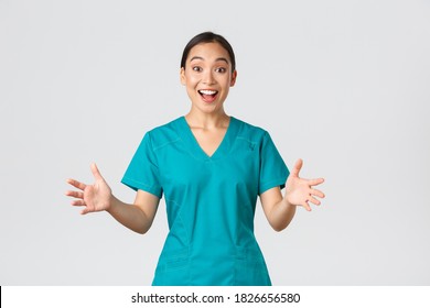 Covid-19, Healthcare Workers, Pandemic Concept. Happy And Surprised Asian Nurse In Scrubs Raising Hands Excited And Smiling. Doctor Congratulate With Great News, Applause, White Background