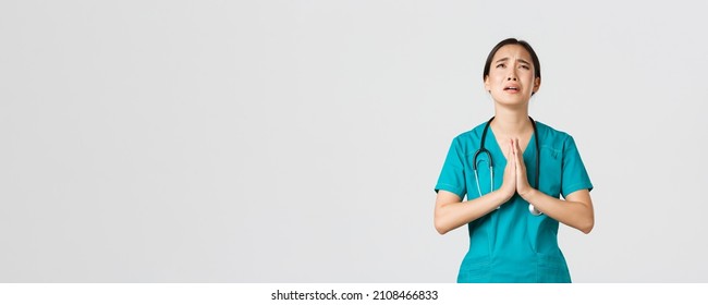 Covid-19, healthcare workers, pandemic concept. Overworked sad and tired asian female doctor, nurse begging for help, pleading god and crying from stress, standing white background - Powered by Shutterstock