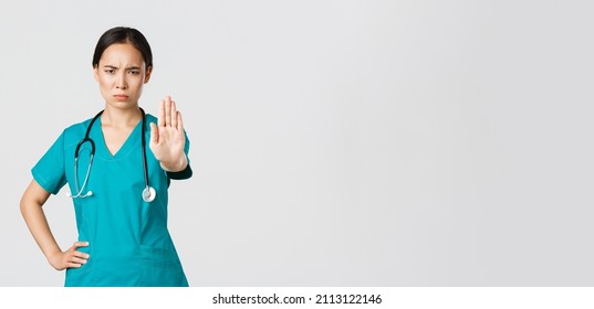 Covid-19, healthcare workers, pandemic concept. Angry serious-looking asian doctor, female physician or nurse in scrubs frowning displeased, extend hand to show stop, disagree, prohibit or forbid - Shutterstock ID 2113122146