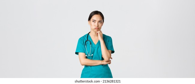 Covid-19, Healthcare Workers, Pandemic Concept. Annoyed And Bothered Asian Female Doctor, Nurse On Her Shift Looking Irritated Or Tired, Eye Roll Bored And Exhale, Standing White Background In Scrubs