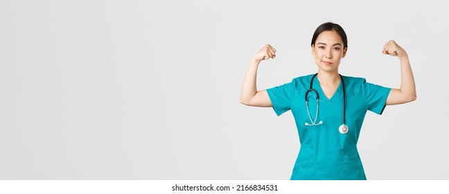 Covid-19, Healthcare Workers And Preventing Virus Concept. Confident Professional Asian Female Doctor, Nurse In Scrubs Smiling Sassy And Flex Biceps, Being Strong, Show-off Muscles