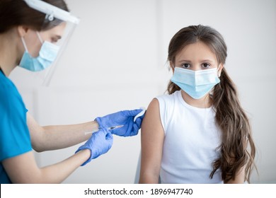 Covid-19 Immunization Campaign. Little Patient In Face Mask Receiving Coronavirus Vaccine Shot From Nurse At Clinic. Child Getting Vaccinated Against Infectious Disease, Protected From Virus