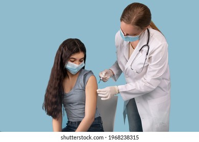 Covid-19 immunization concept. Teenage girl being vaccinated against coronavirus on blue studio background. Young doctor giving antiviral vaccine injection to adolescent patient - Shutterstock ID 1968238315