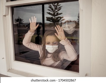 COVID-19 Lockdown. Depressed Lonely Little Girl With Face Mask Looking Through The Window During Quarantine. Sad Sick Child In Self Isolation At Home. Coronavirusu Outbreak And Children Mental Health.