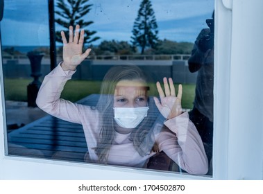 COVID-19 Lockdown. Depressed Lonely Little Girl With Face Mask Looking Through The Window During Quarantine. Sad Sick Child In Self Isolation At Home. Coronavirusu Outbreak And Children Mental Health.