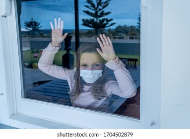 COVID-19 Lockdown. Depressed Lonely Little Girl With Face Mask Looking Through The Window During Quarantine. Sad Sick Child In Self Isolation At Home. Coronavirusu Outbreak And Children Mental Health.