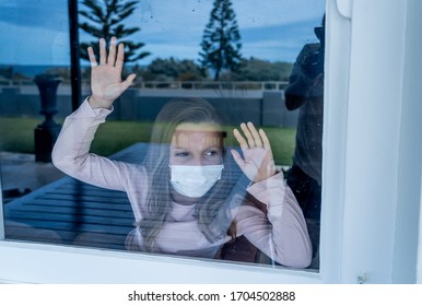 COVID-19 Lockdown. Depressed Lonely Little Girl With Face Mask Looking Through The Window During Quarantine. Sad Sick Child In Self Isolation At Home. Coronavirusu Outbreak And Children Mental Health.