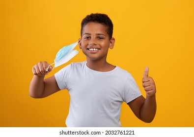 COVID-19 lockdown, pandemic restrictions for kids, children, teens cocnept. Cheerful preteen black boy taking off his protective face mask, showing thumb up, yellow studio background, copy space - Powered by Shutterstock