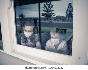 COVID-19 Lockdowns. Sad Children With Face Mask Looking Through The Window During Quarantine At Home. Kids Feeling Sad As School Is Closed. Coronavirus Outbreak Isolation And Kids Mental Health.