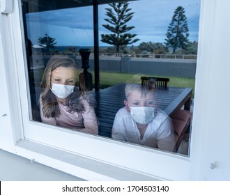 COVID-19 Lockdowns. Sad Children With Face Mask Looking Through The Window During Quarantine At Home. Kids Feeling Sad As School Is Closed. Coronavirus Outbreak Isolation And Kids Mental Health.