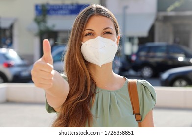 COVID-19 Optimistic Young Woman Wearing Protective Mask KN95 FFP2 Avoiding Coronavirus Disease 2019 Showing Thumbs Up In City Street