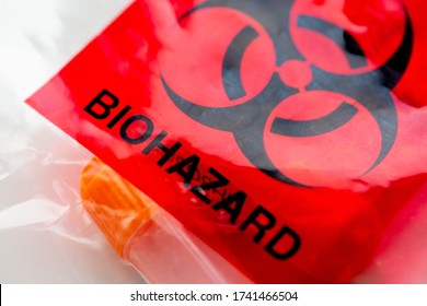 Covid-19 Outbreak. Biohazard Black Sign And Symbol On The Red Background On The Plastic Bag With A Plastic Vial With A Biological Specimen. Concept Of Coronavirus Test, Infecious Diseases. Red Waste.