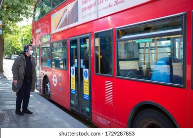 Covid-19 Outbreak Red Double Decker Bus And Male Passenger Standing At Bus Stop Wearing Face Mask. Safety Guidelines Stickers On The Bus. Concept Of TFL, Essential Travel. London, UK 11/05/2020