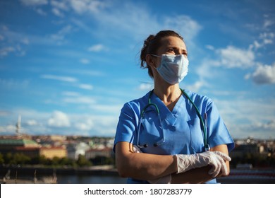 Covid-19-Pandemie. selbstbewusste moderne Ärztin in Skrupeln mit Stethoskop, medizinischer Maske und Gummihandschuhen, die in die Ferne der Stadt gegen den Himmel schauen.