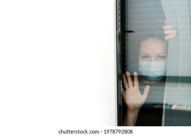 COVID-19 Pandemic Coronavirus Lockdown. Sad Woman On Quarantine In Medical Mask On Face Looking Through The Window. People On Self Isolation Concept