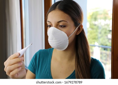 COVID-19 Pandemic Coronavirus Mask Fever Worry Woman Checking Temperature With Thermometer At Home Symptom Of SARS-CoV-2. Girl With Mask On Face Check Fever One Of Symptoms Of Coronavirus Disease 2019