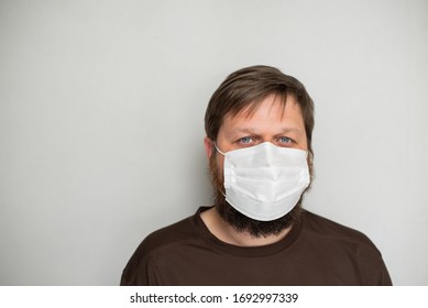 COVID-19 Pandemic Coronavirus. Portrait Of A Man With A Beard In A White Mask On A Light Background