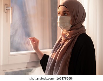 COVID-19 Pandemic Coronavirus Woman With Hijab With Wearing Face Mas  Looks Out The Window Isolation. Arab Woman Hijab.