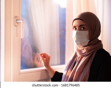 COVID-19 Pandemic Coronavirus Woman With Hijab With Wearing Face Mas  Looks Out The Window Isolation. Arab Woman Hijab.