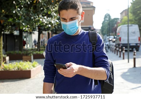COVID-19 Pandemic Coronavirus Worried Young Man Wearing Surgical Mask Using Smart Phone App in City Street to Aid Contact Tracing and Self Diagnostic in Response to the Coronavirus Pandemic 2019