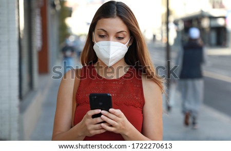 COVID-19 Pandemic Coronavirus Young Woman Wearing KN95 FFP2 Mask Using Smart Phone App in City Street to Aid Contact Tracing in Response to the 2019-20 Coronavirus Pandemic