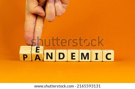Covid-19 pandemic or endemic symbol. Doctor turns wooden cubes and changes the concept word pandemic to endemic. Beautiful orange background copy space. Medical Covid-19 pandemic or endemic concept.