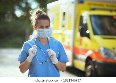 Covid-19 Pandemic. Modern Paramedic Woman In Scrubs With Stethoscope And Medical Mask Outside Near Ambulance.