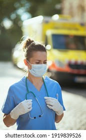 Covid-19 Pandemic. Modern Paramedic Woman In Scrubs With Stethoscope And Medical Mask Outside Near Ambulance.