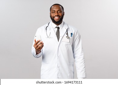 Covid19, Pandemic And Online Medicine Concept. Handsome African-american Male Doctor, Physician Contact His Patients Via Smartphone App, Smiling Camera, People Staying Home But Use Healthcare Service