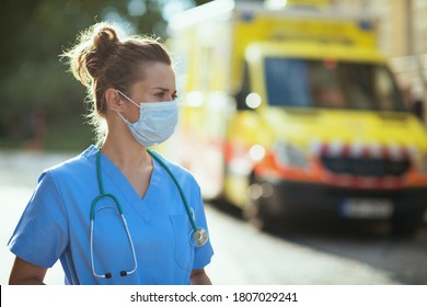 Covid-19 Pandemic. Pensive Modern Medical Doctor Woman In Uniform With Stethoscope And Medical Mask Outside Near Ambulance.